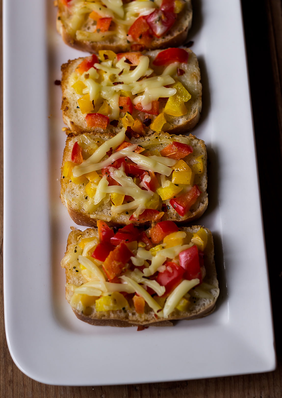 Grated cheese and chili flakes being sprinkled over buttered bread