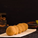 Placing freshly rolled besan ladoos on a serving tray.