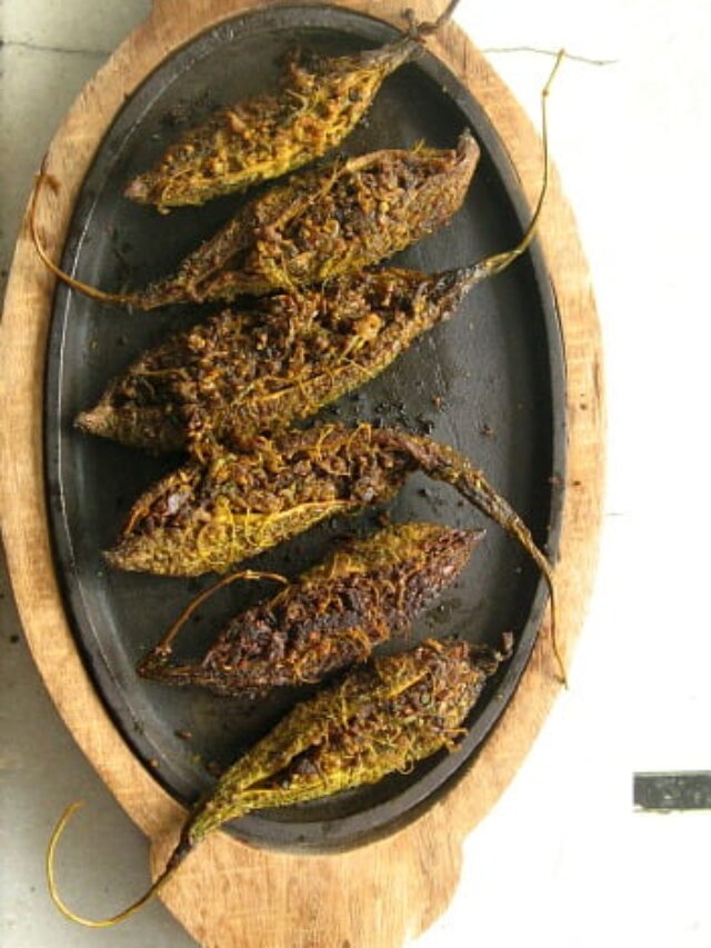 Golden brown stuffed karela cooking on a wooden plate