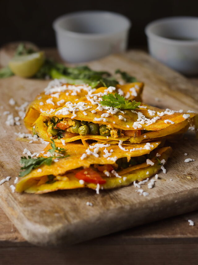 Stack of moong dal chillas served on a plate garnished with grated paneer