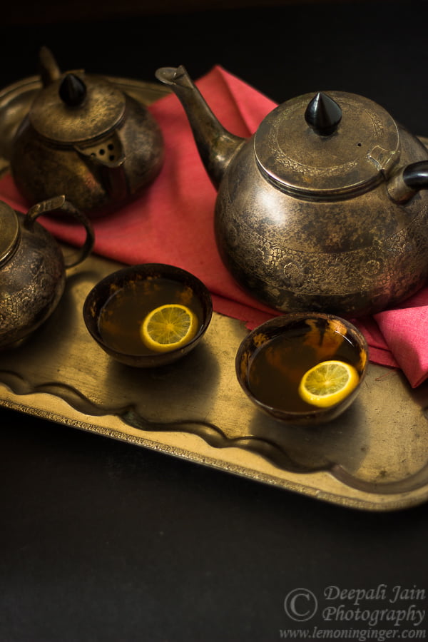 Two glasses filled with hot lemon tea with a teapot