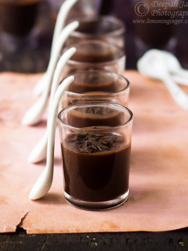 Multiple glasses of dark chocolate mousse lined up on a wooden tray, topped with grated chocolate