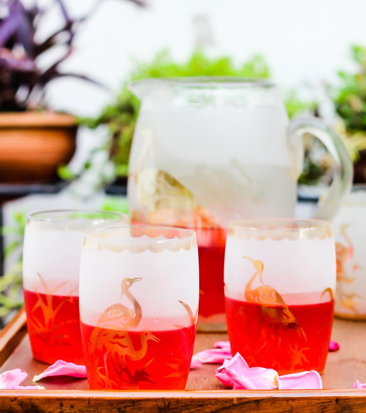 A glass of Rooh Afza Sharbat placed on a wooden table with scattered rose petals