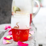A glass of Rooh Afza Sharbat placed on a wooden table with scattered rose petals