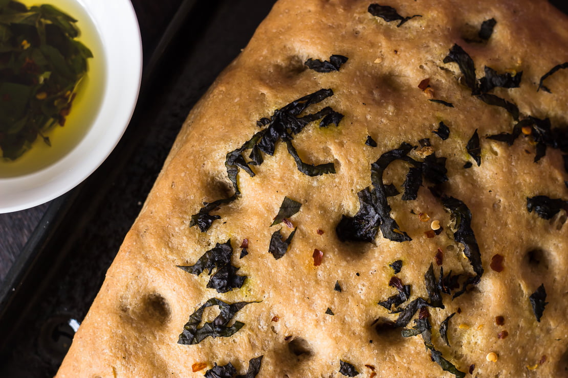 Close-up of golden crust and basil topping on whole wheat focaccia bread