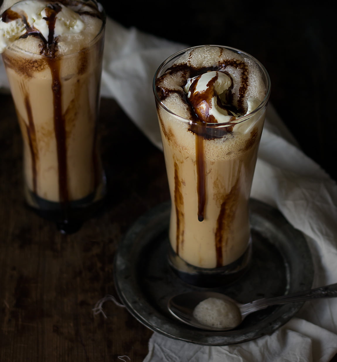 Close-up of an iced coffee frappe with a thick layer of whipped cream and chocolate syrup drizzling down the sides