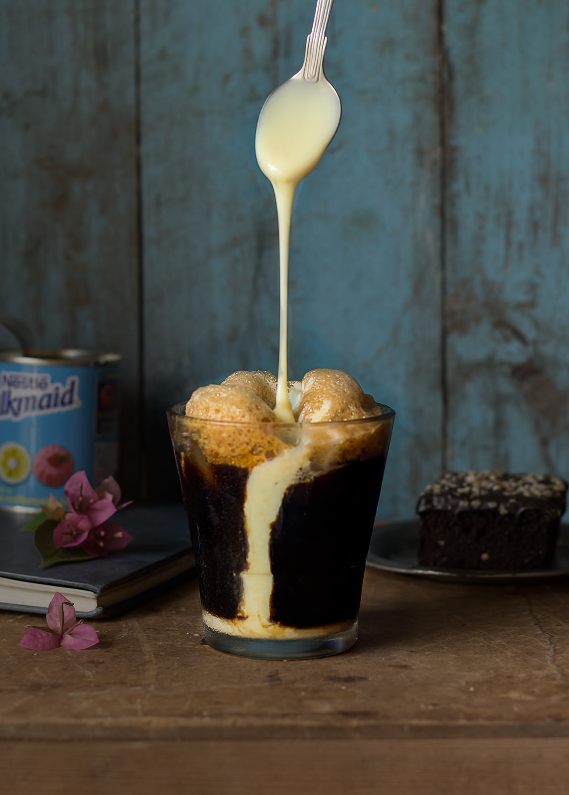 A tall glass of iced coffee with a frothy top and a straw