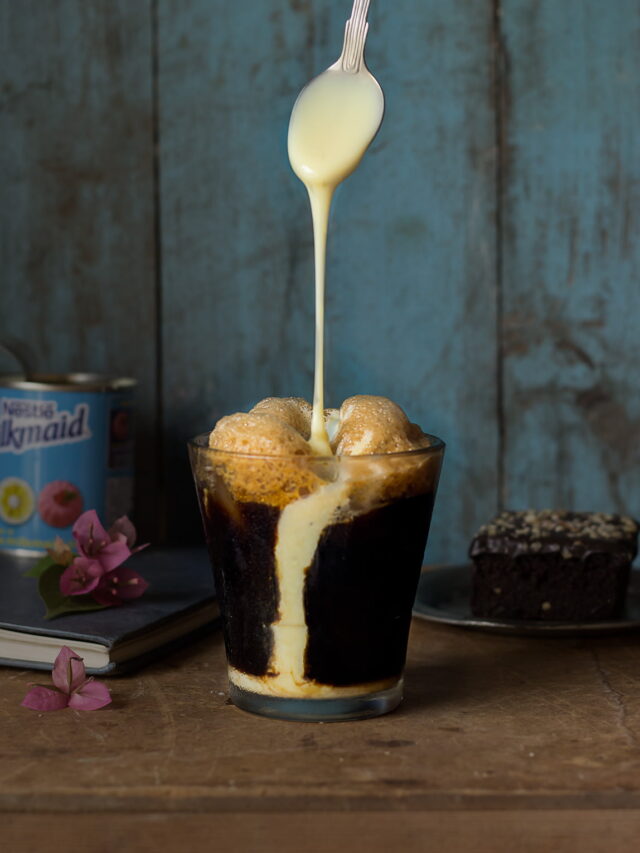 A tall glass of iced coffee with a frothy top and a straw