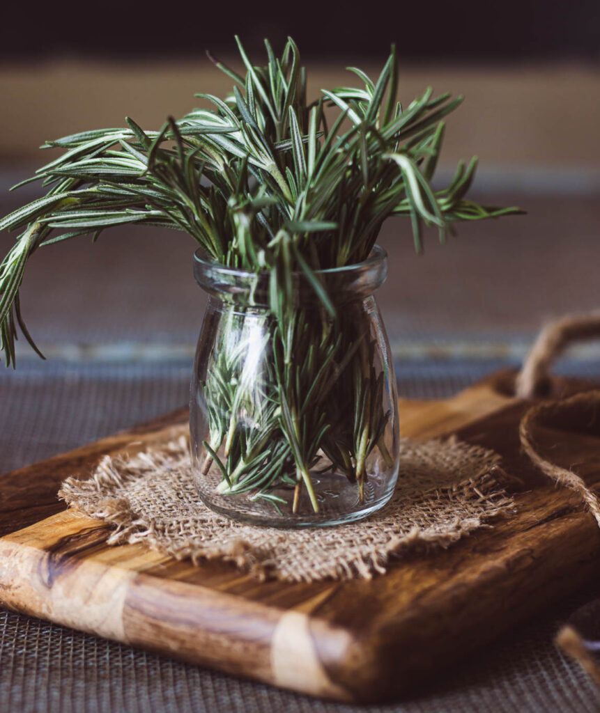 A close-up of dried rosemary leaves in a glass jar