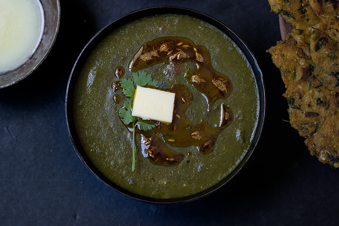 A bowl of rich and creamy Sarson Ka Saag topped with butter, served hot in Punjabi style